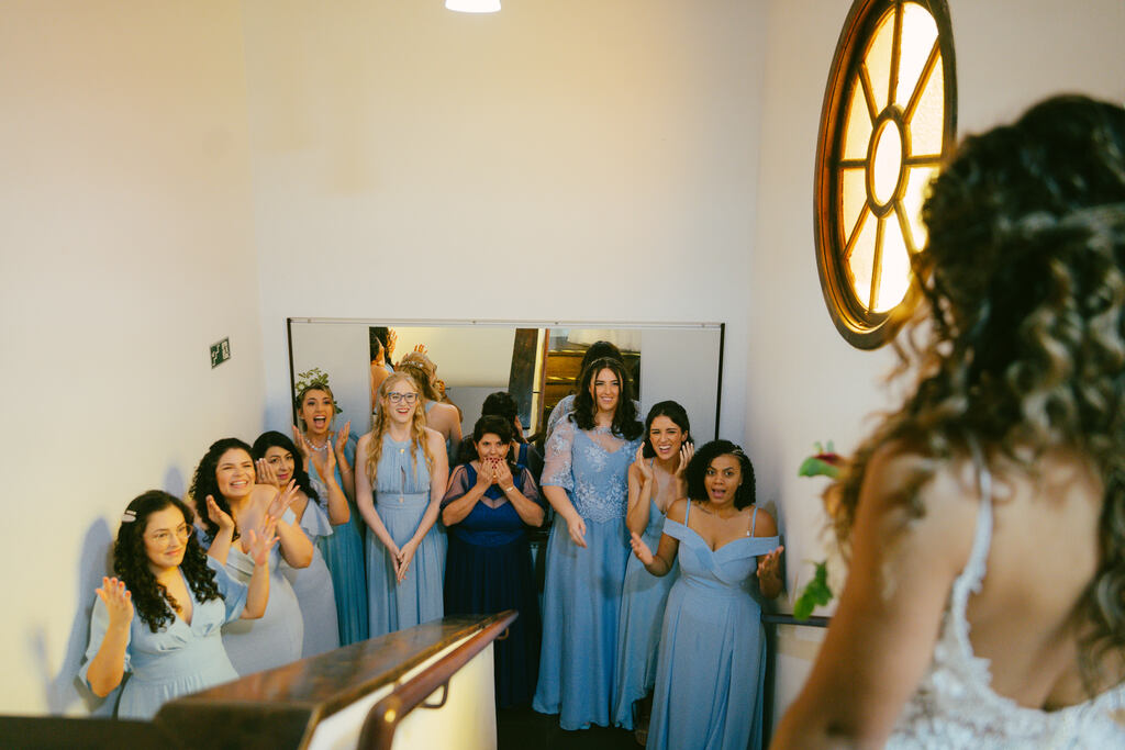 noiva no topo da escada e madrinhas com vestidos azuis serenity reagindo ao first look com a noiva