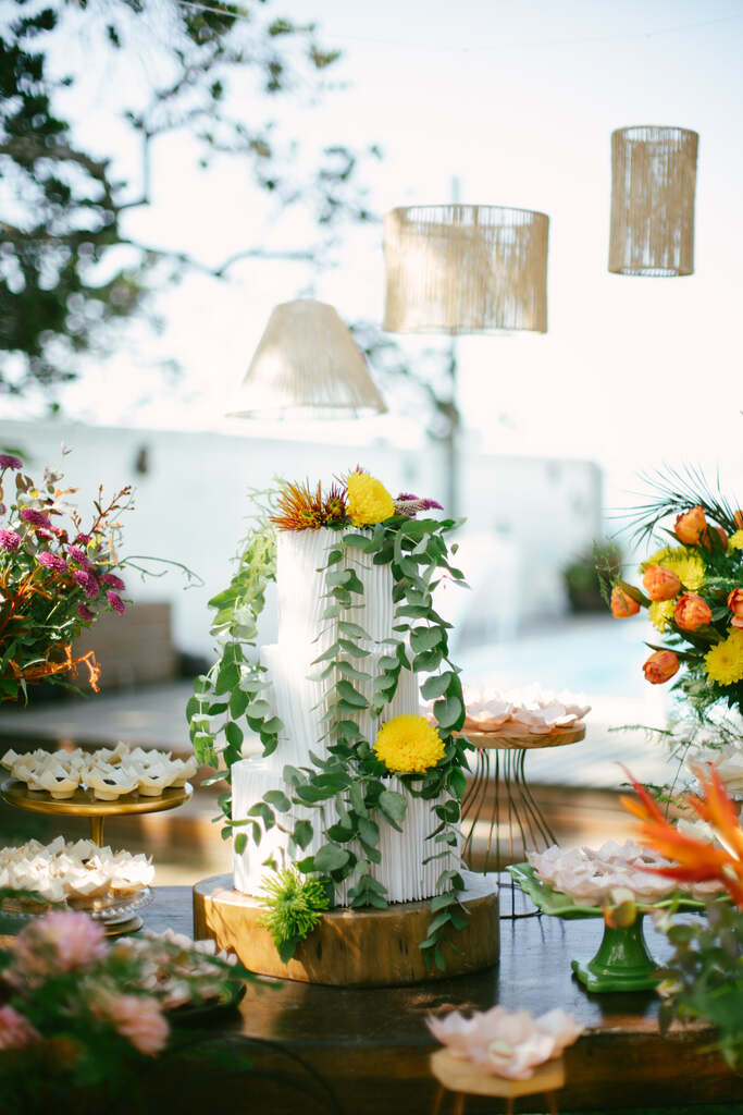 mesa com bolo de casamento branco com três andares com flores amarelas e plantas pendentes