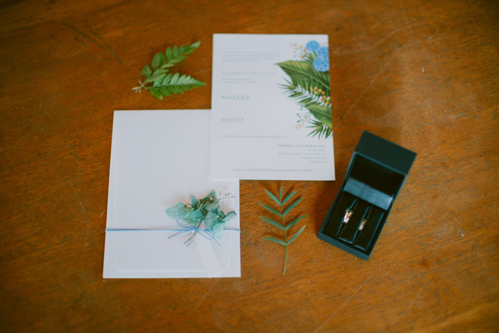 convites de casamento branco com estampa com plantas na lateral ao lado da caixinha preta com alianças