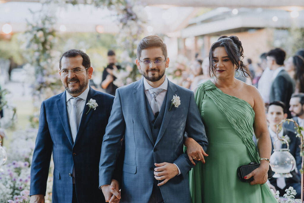 entrada do noivo com terno azul ao lado do pai e da mãe com vestido verde sage