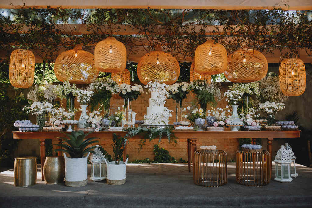mesa de madeira com bolo de casamento branco com flores e vários vasos com flores 