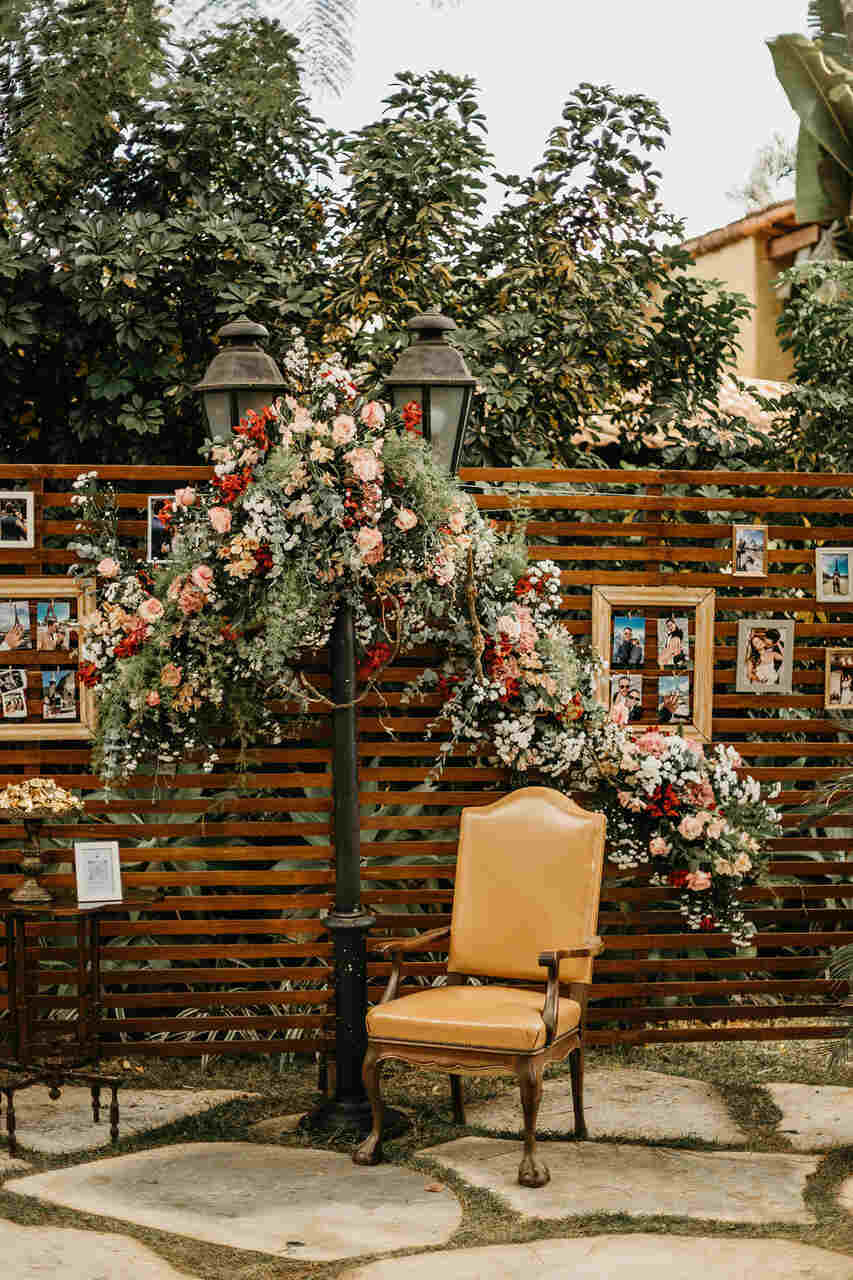 backdrop de madeira com retratos e cadeira clássica bege ao lado de poste de luz antigo decorado com flores brancas rosas e vermelhas