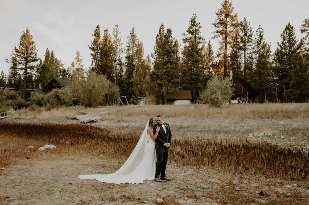 Noiva abraçando o noivo em meio ao ar livre, em uma paisagem com árvores e folhas secas