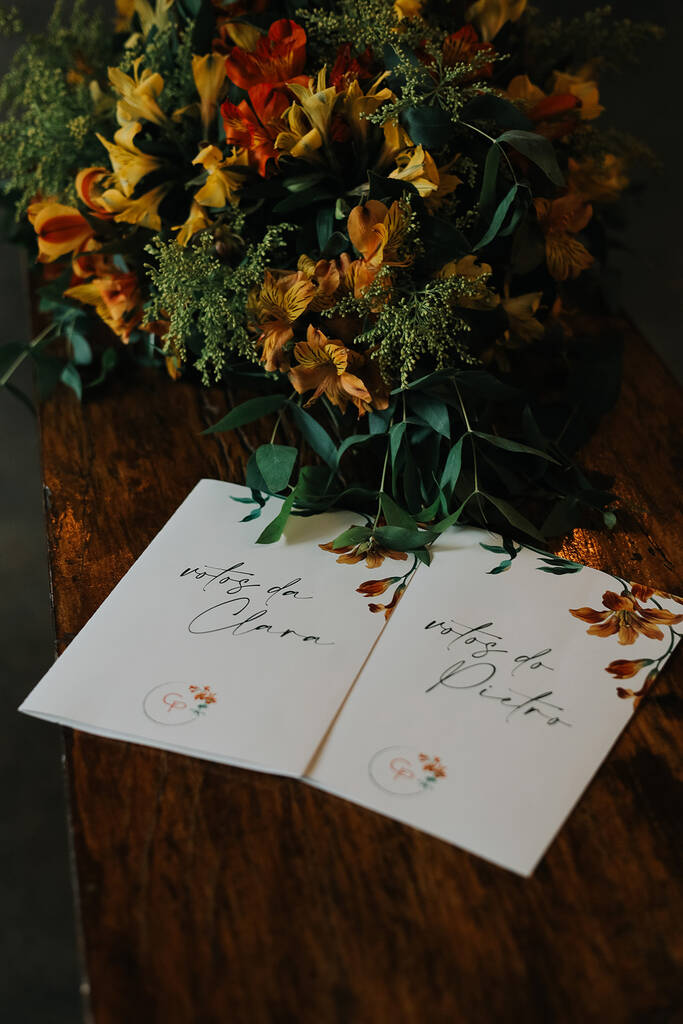 caderno de votos branco com desenhos de flores na lateral em cima da mesa de madeira com flores