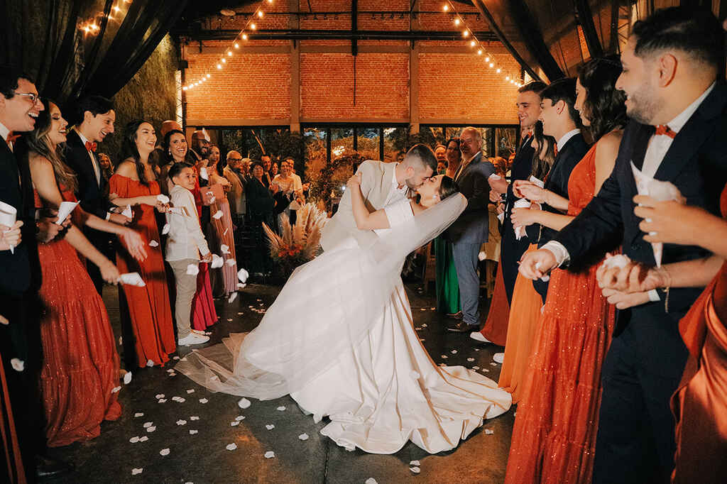 noivos se beijando na saída do casamento sob pétalas brancas