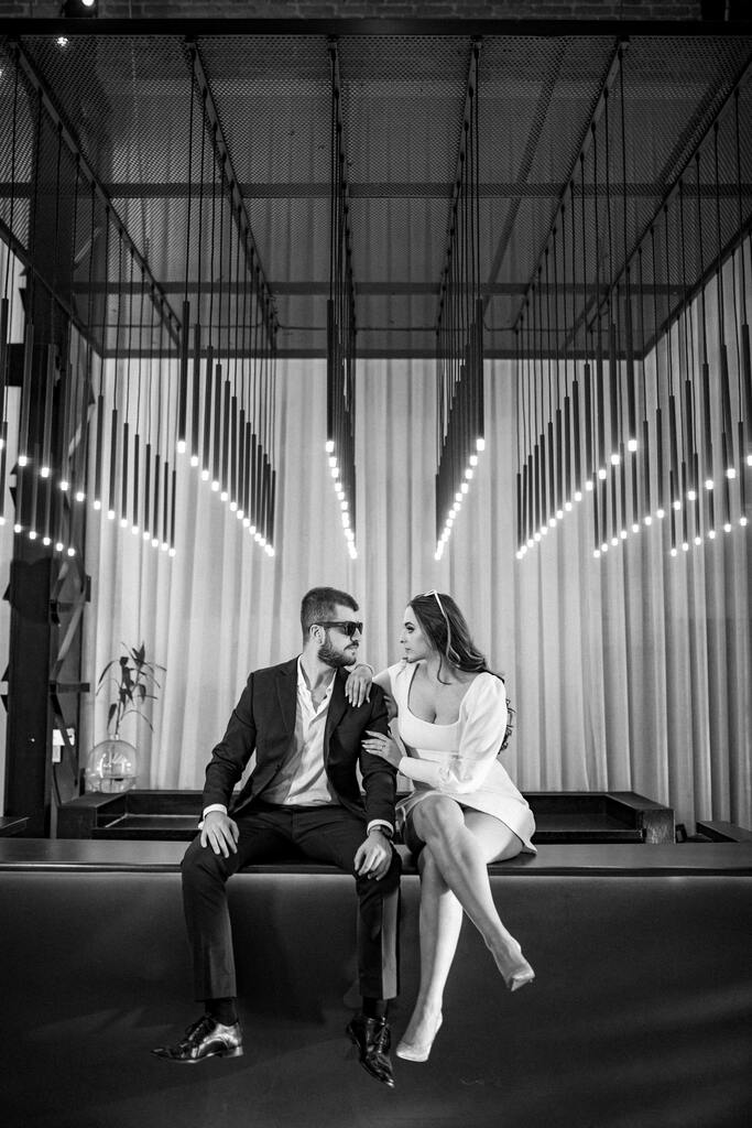 casal sentado no chão e acima fileiras de luminárias modernas