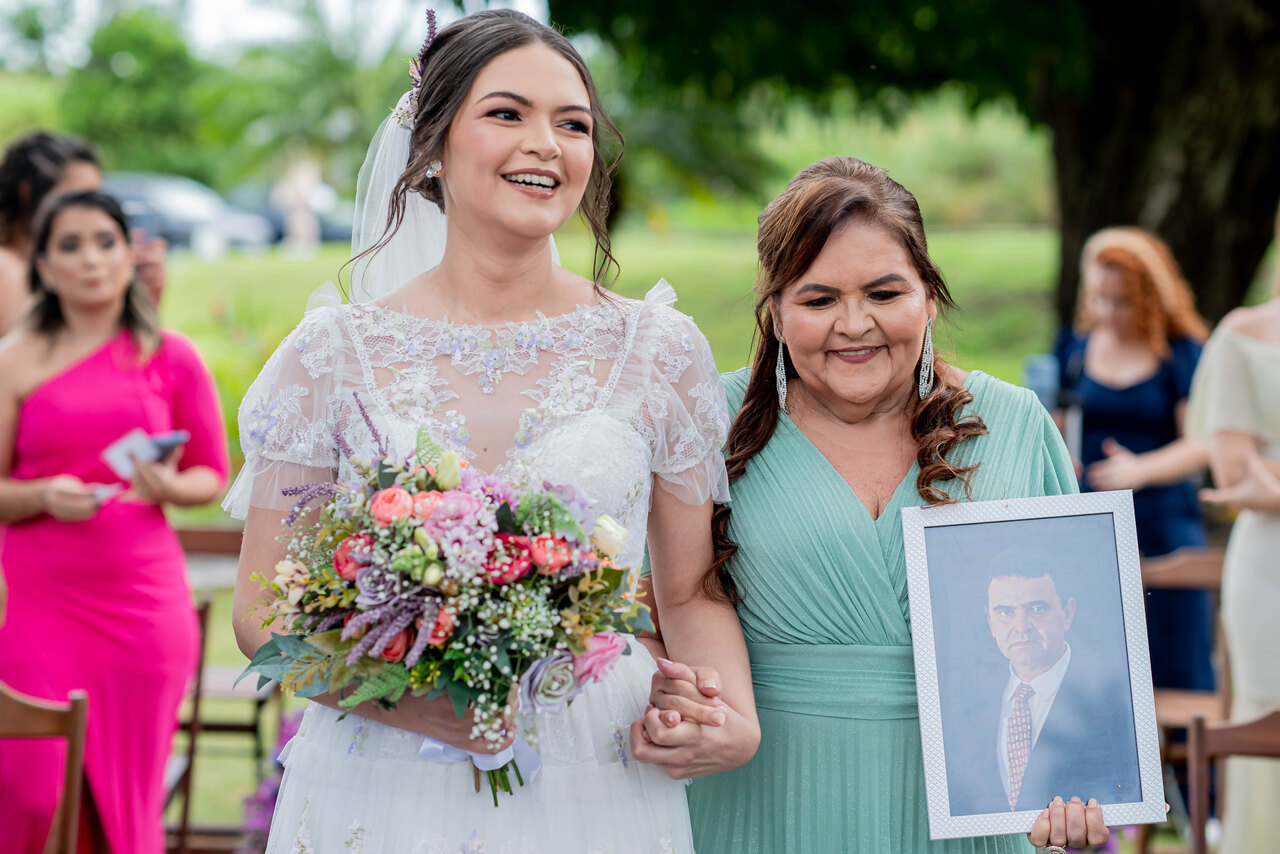 entrada da noiva com buquÊ colorido ao lado da mãe com vestido verde claro segurando retrato com foto do pai