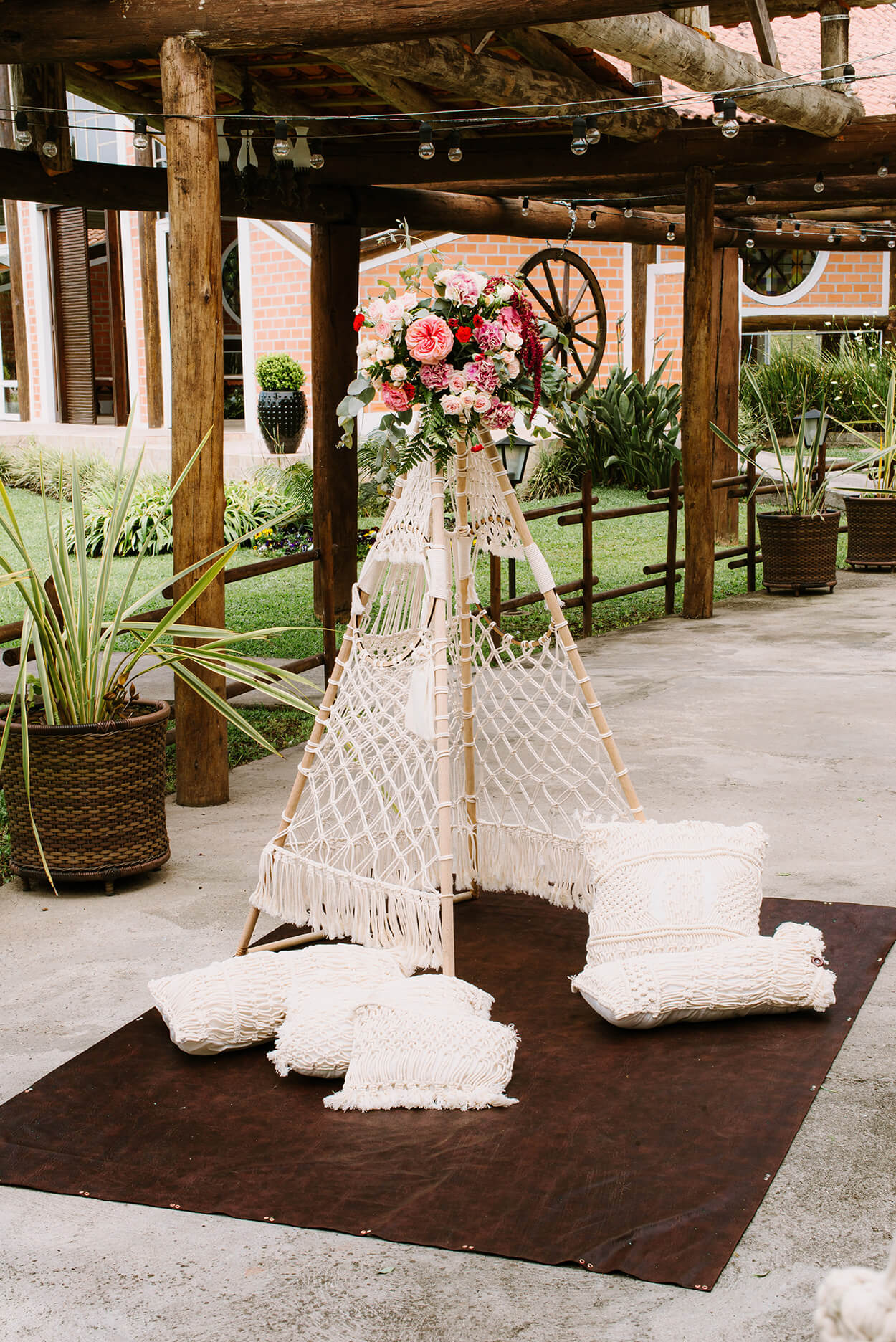 cabana feita com macrame com flores brancas e rosas no topo e almofadas brancas no chão