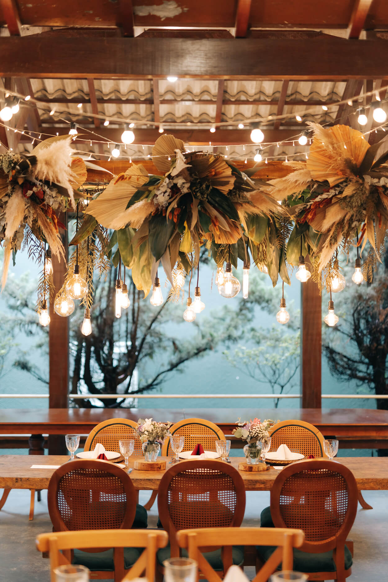 luminária com capum dos pampas e palmeira seca suspensa em cima de mesa posta