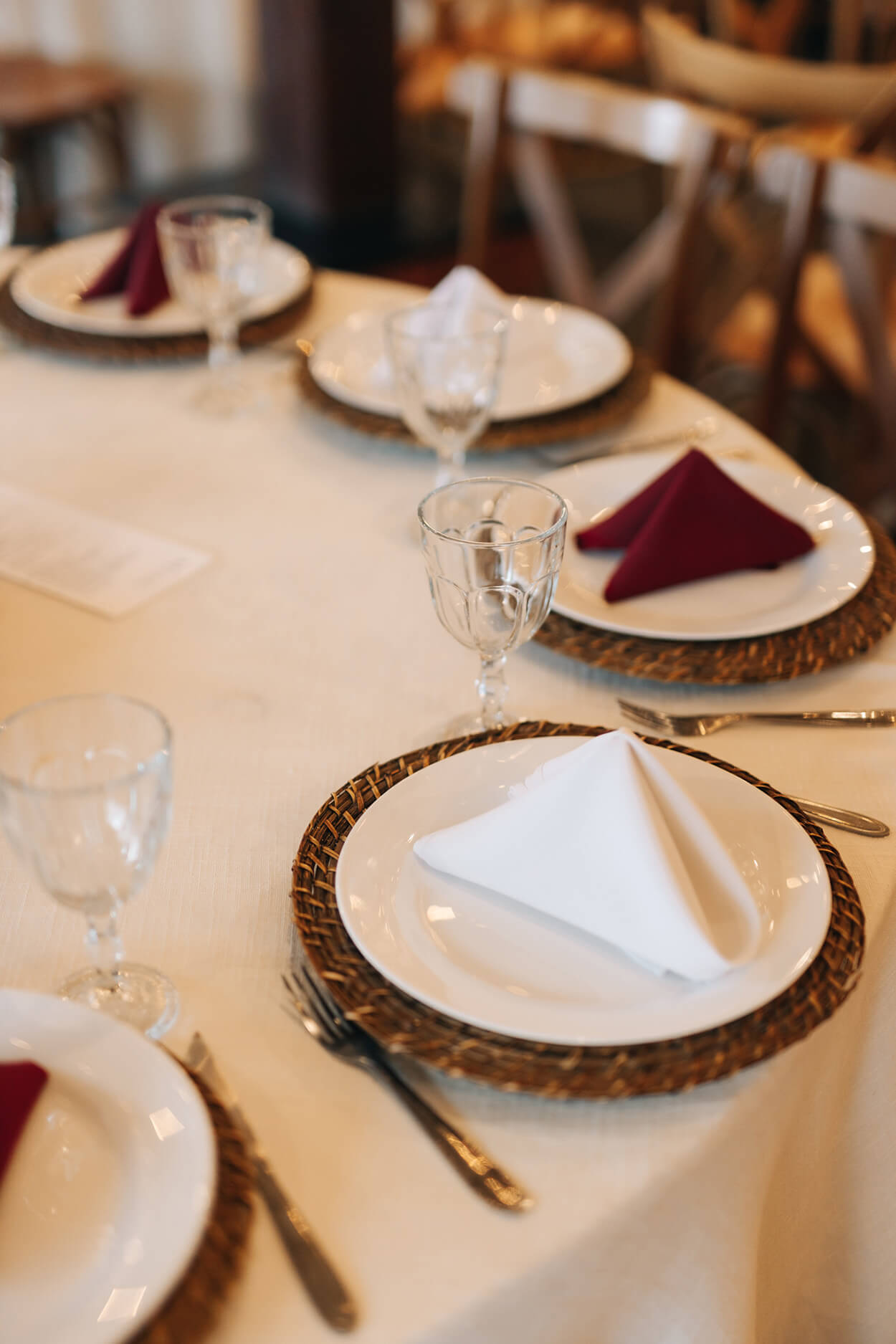 mesa redonda posta com tolaha branca e sousplat de palha com pratos com guardanapos brancos e marsalas