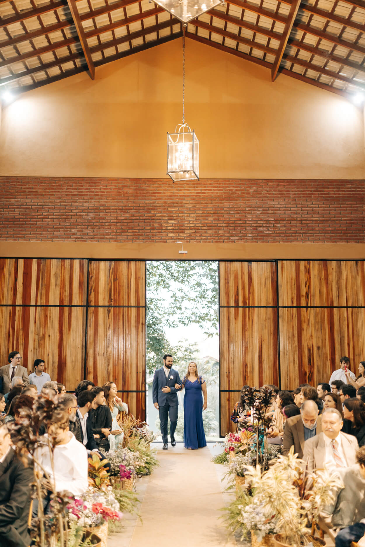 entrada do noivo ao lado da mãe com vetsido azul no salão para cerimônia de casamento