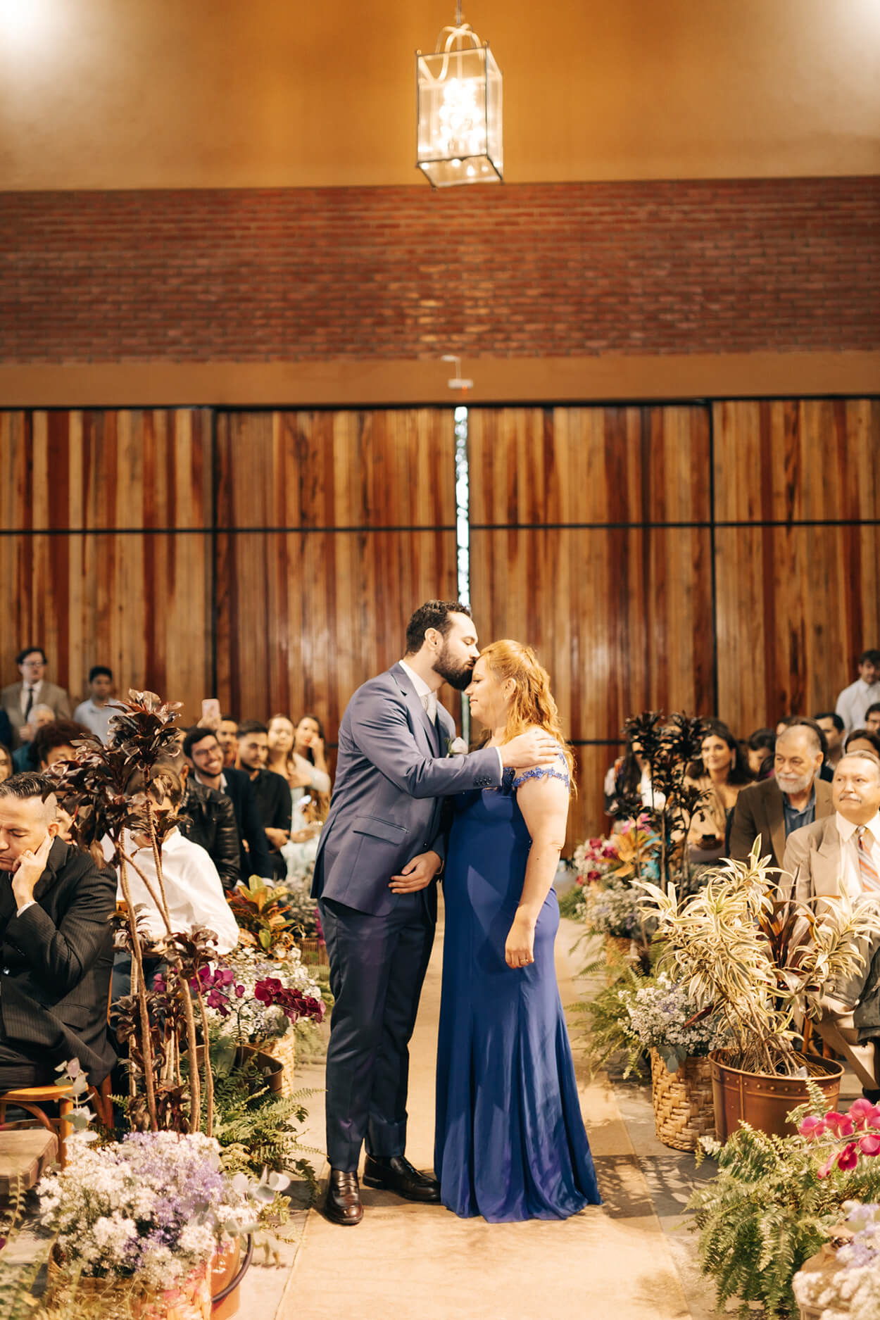 noivo beijando a testa da mãe com vestido azul no salão para cerimônia de casamento