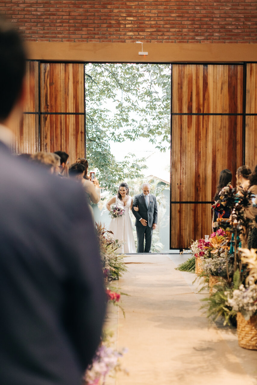 entrada da noiva ao lado do pai com terno cinza no salão rústico