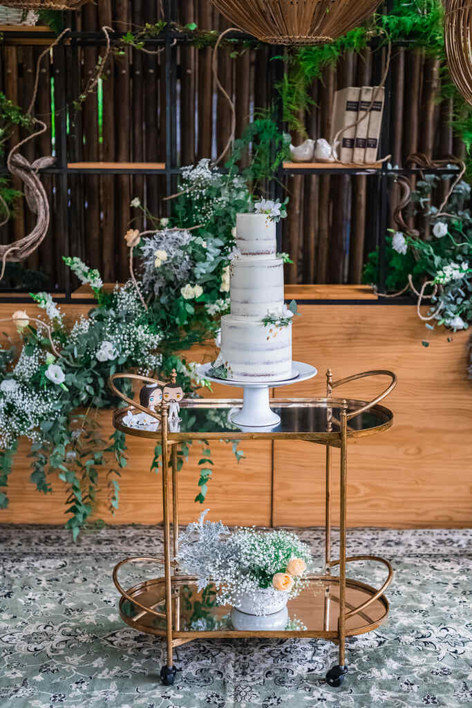 salão rústico com mesa de madeira com arranjos florais brancos e mesinha com bolo de casamnento de três andares