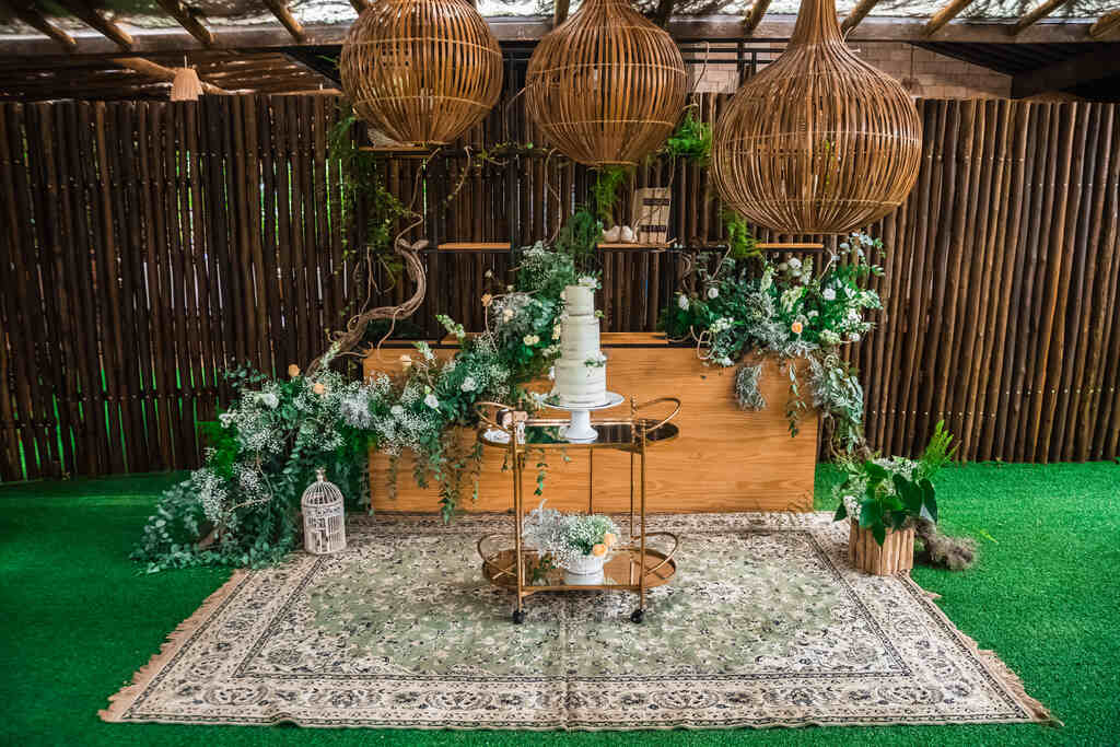 salão rústico com mesa de madeira com arranjos florais brancos e mesinha com bolo de casamnento de três andares