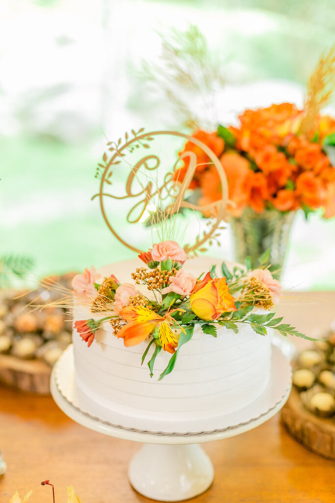 bolo de casamento branco espatulado com flores rosas e laranjas e topo com iniciais dos noivos em madeira