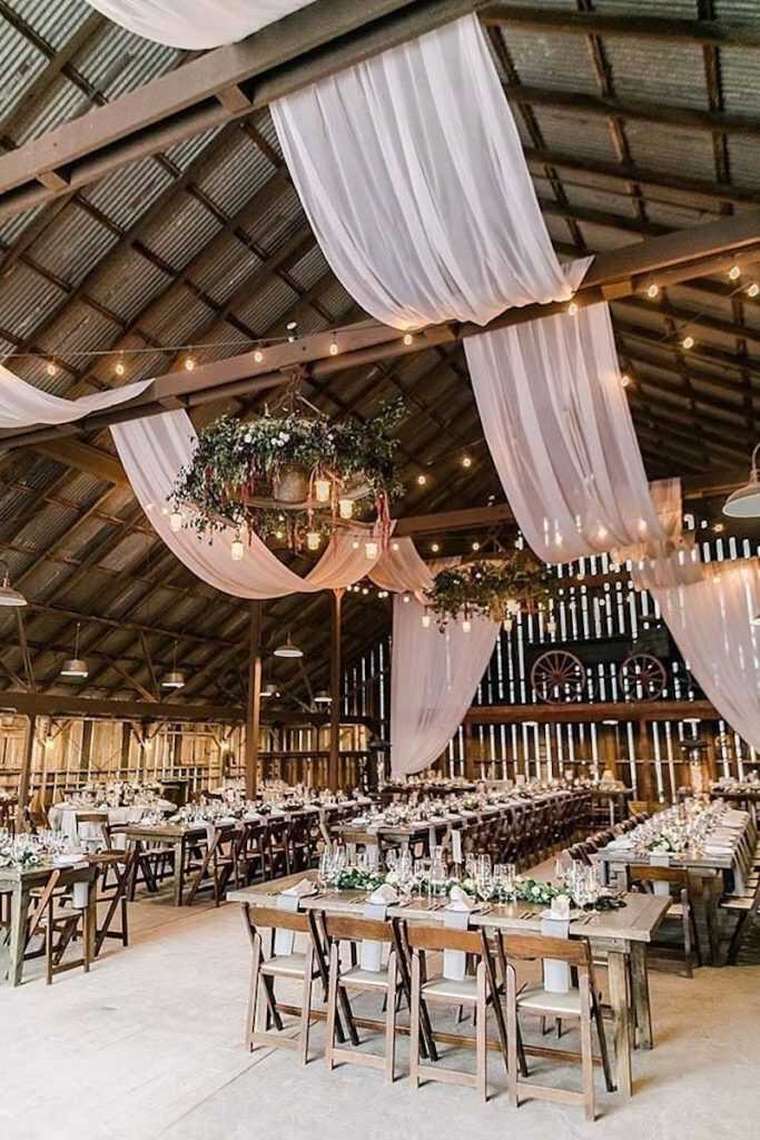 salão rústico decorado com tecidos brancos e luzinhas no teto com mesas postas