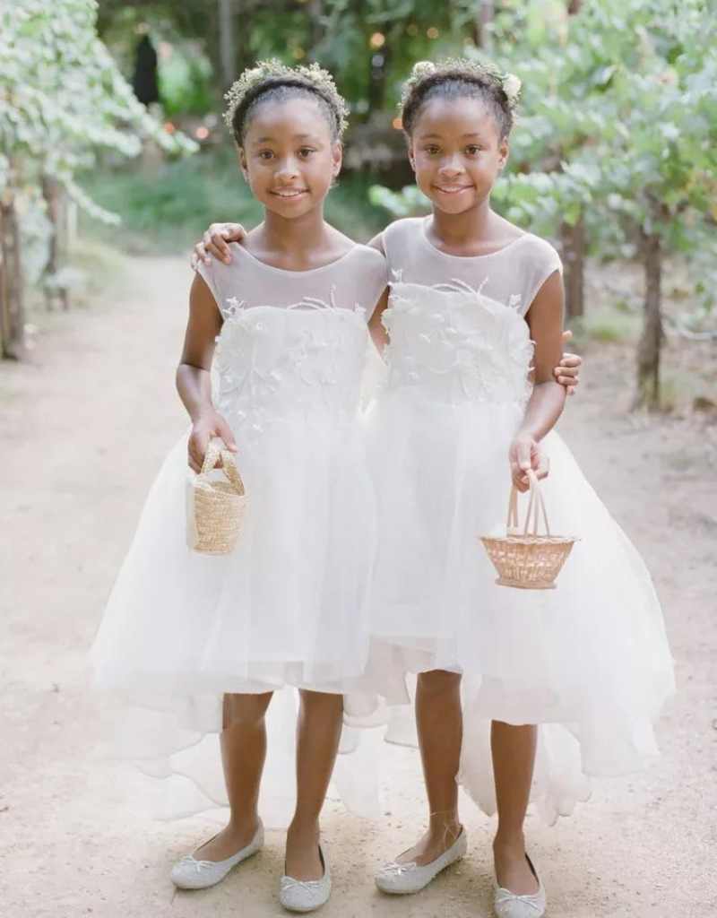 duas floristas de casamento com vestido branco, sapatilhas, cabelo preso e mini cestinhos de flores