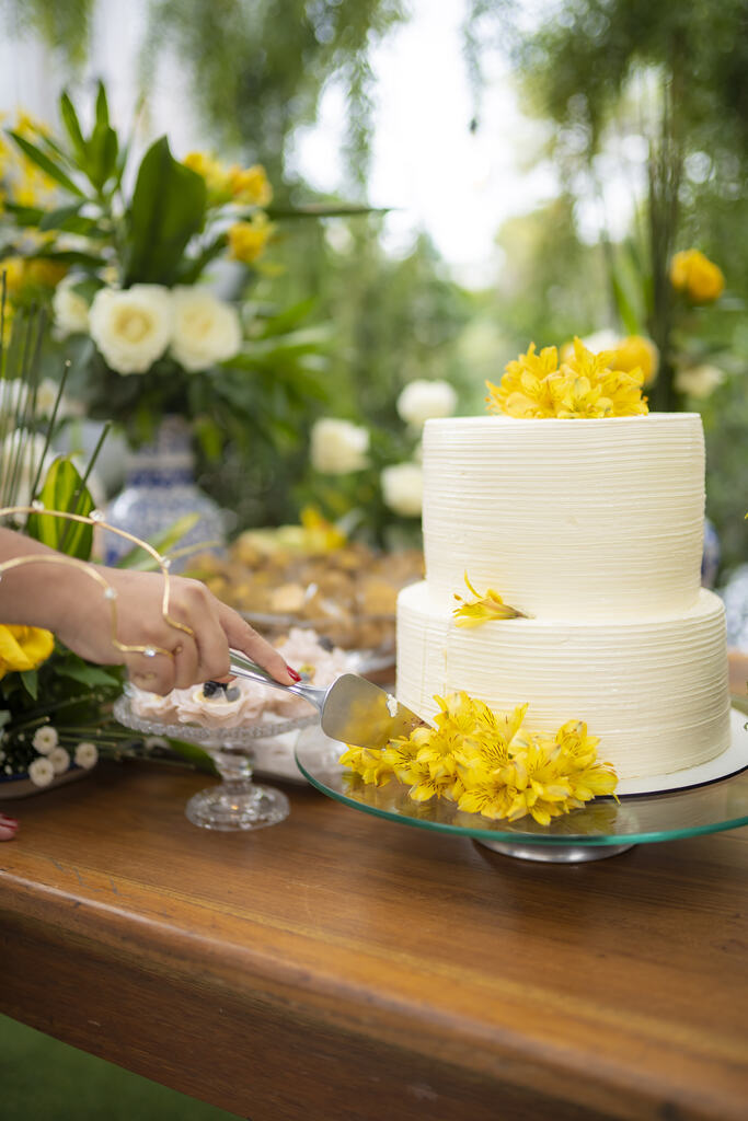 noiva cortando bolo de casamento branco espatulado com flores amarelos no topo