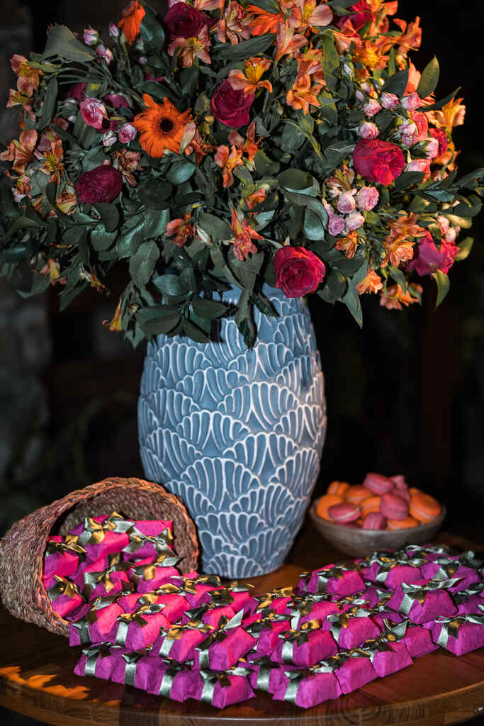 vaso azul com flores coloridas e bem-casados com emabalagens cor de rosa em cima da mesa