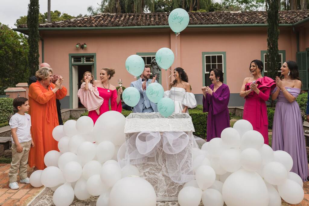 noivos e convidados ao redor de caixa ddecorada com balões brancos e balões azuis voando para chá revelação 