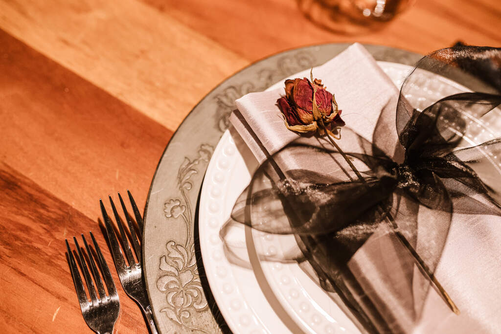 mesa posta com sousplat de prata com guardanapo branco com rosa seca e laço com tecido preto e transparente