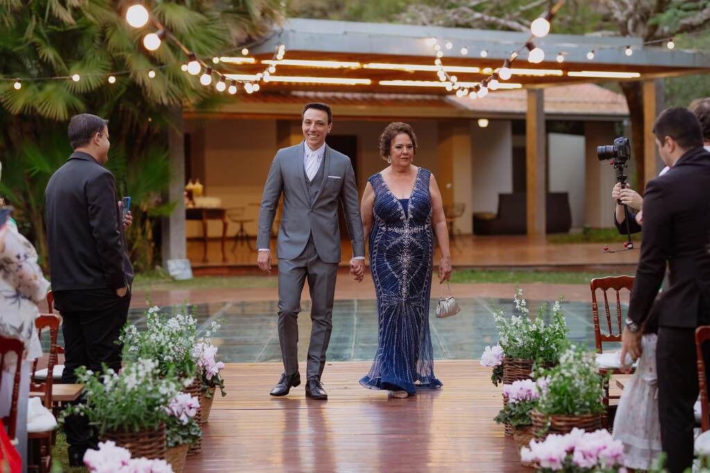 entrada do noivo com terno cinza com colete ao lado da mãe com vetsido azul 