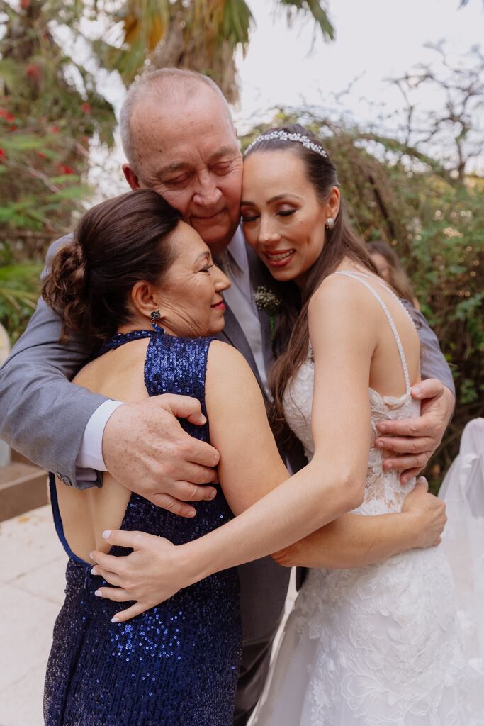 pai da noiva abraçando a filha e a esposa com vestido azul escuro com brilho
