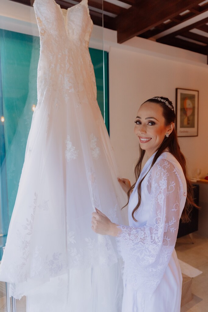 mulher com robe branco e tiara olhando o seu vestido de noiva