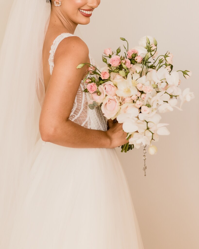 noiva de lado com vestido segurando buquê com orquideas brancas e flores cor de rosa e véu longo
