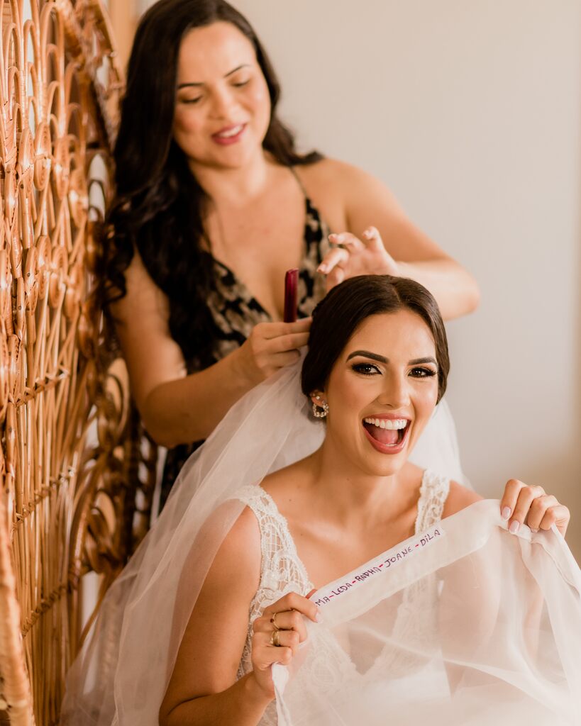 mulher arrumando o cabelo da noiva enquanto ela mostar a barra do vestido bordada