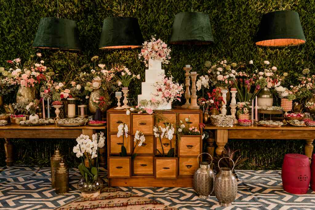 mesas de madeira com bolo de casamento com quatro andare com topo de flores brancas e rosas