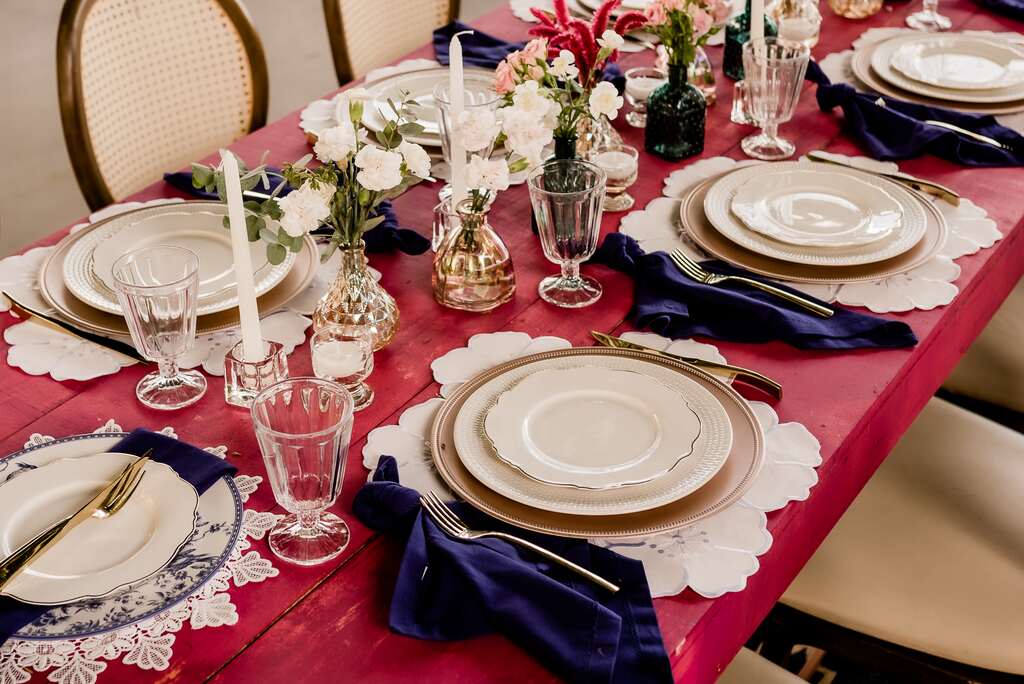 mesa cor de rosa com mesa posta com sousplat bege velas brancas guardanapo azul e flores no centro