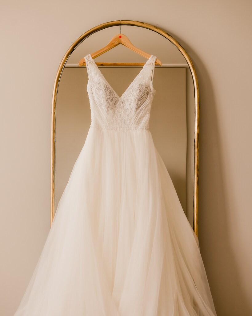 vestido de noiva com decote em V pendurado em cabide de madeira na frente de espelho