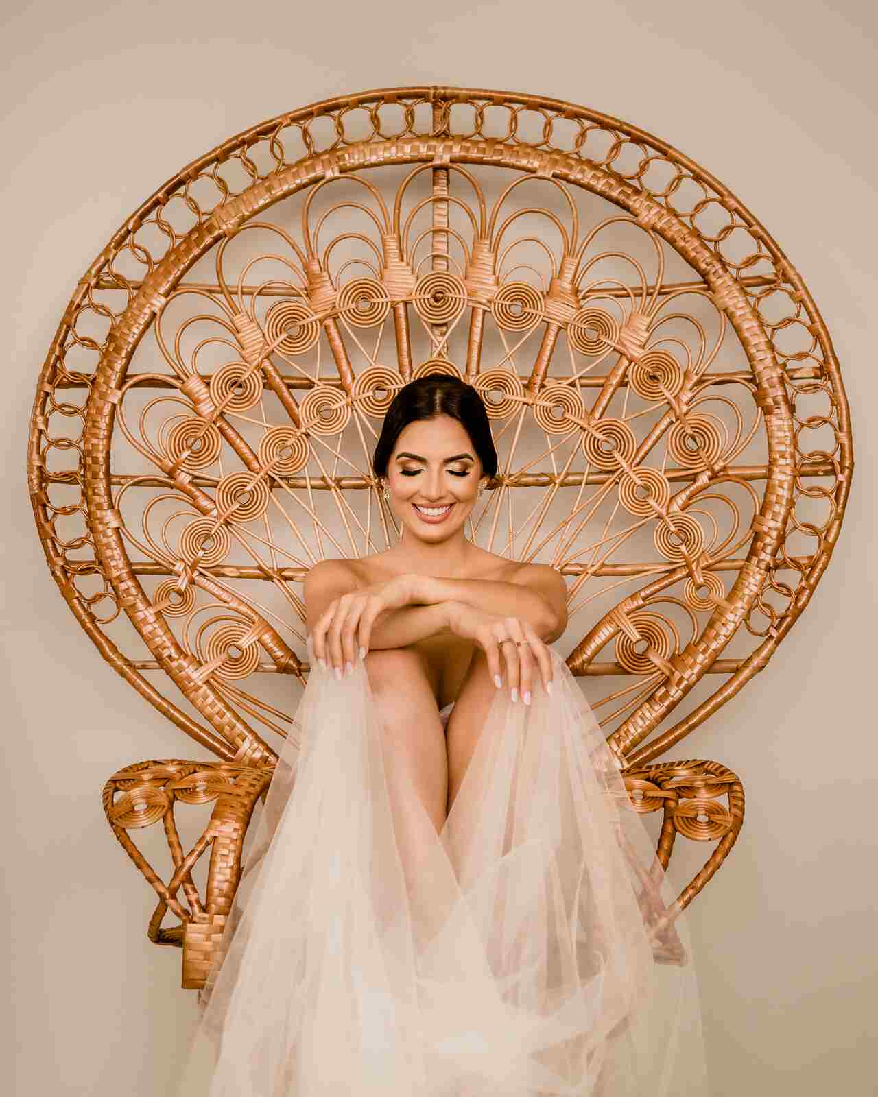 mulher de lingerie segurando véu de noiva sentada em cadeira pavão de palha em ensaio boudoir