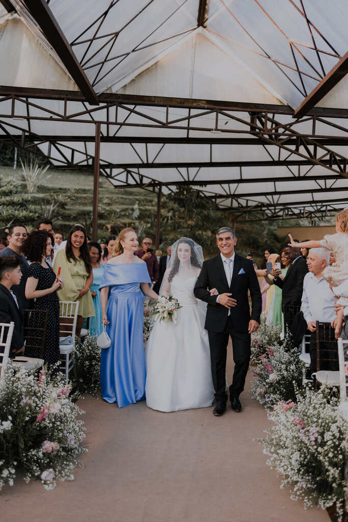 entrada da noiva com véu o lado da mãe com vetsido azul serenity e pai com terno preto
