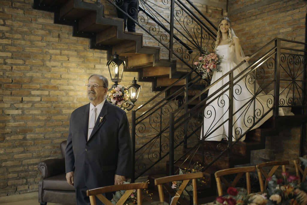 vestido de noiva com buquê rosa descendo as escadas para fazer o first look com o pai com terno preto