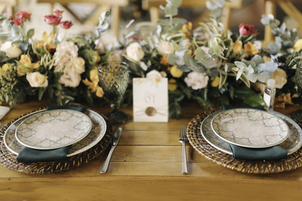 mesa posta com sousplat de palha e prato estampado e flores brancas rosas e amarelas no centro