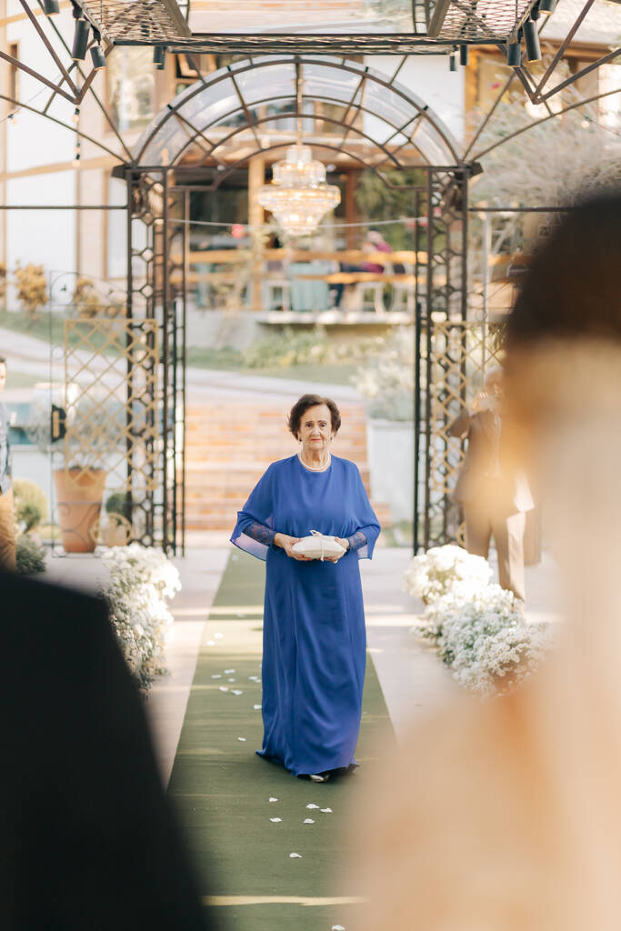 entrada de mulher com vestido azul cobalto carregando o porta alianças
