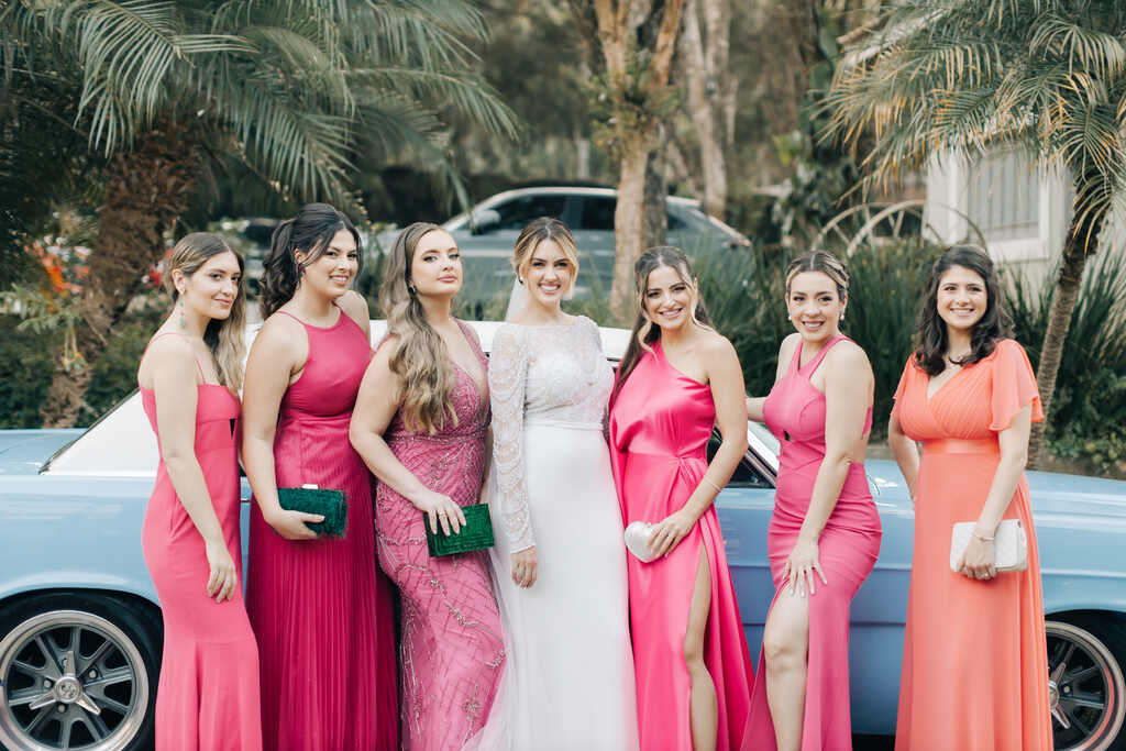 noiva ao lado das madrinhas com vestidos cor de rosa na frente de carro antigo azul