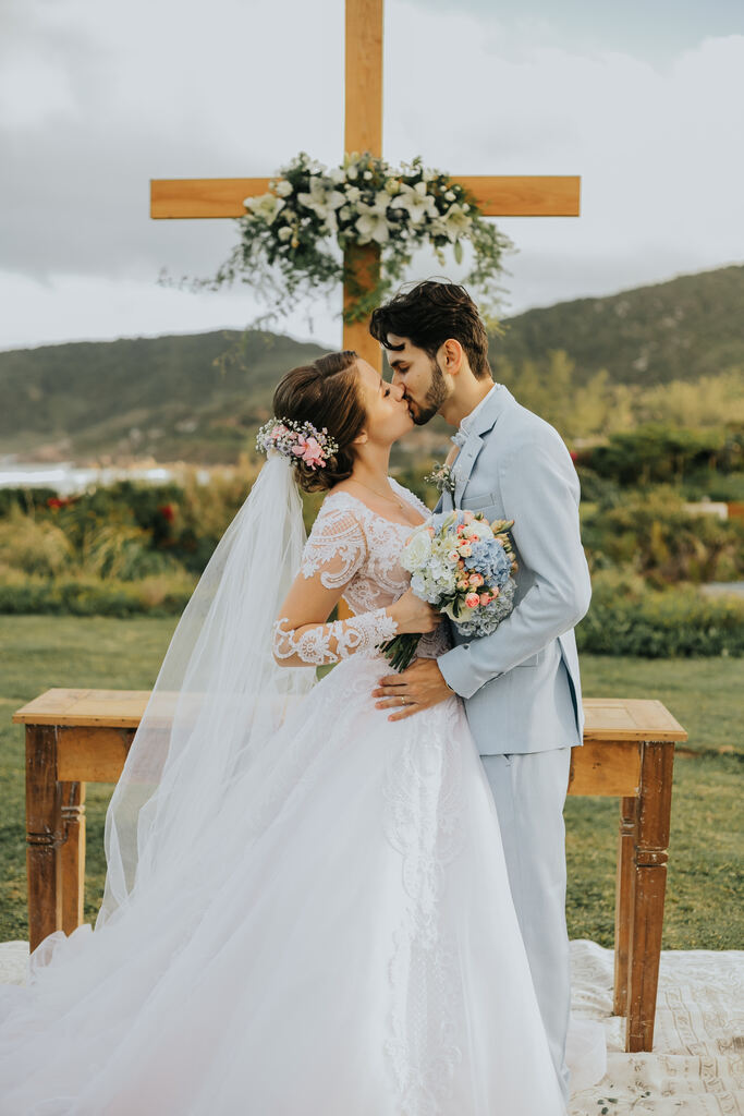 noivos se beijando na frente do altar de madeira em forma de criz com lírios brancos