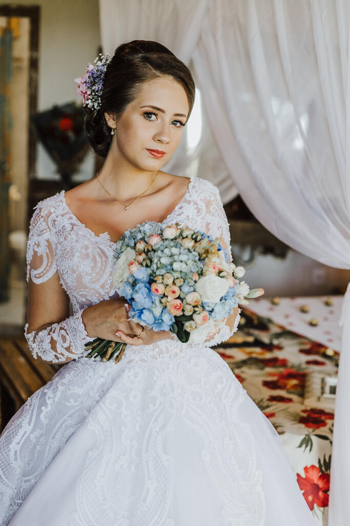 noiva com vestido com decote em v e manga longa segurando buquÊ redondo com hortensias azuis e flores brancas e rosas