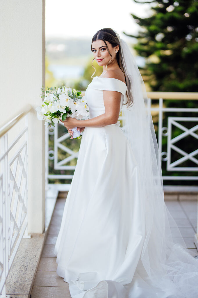 noiva com vestido minimalista segurando buquê com flores brancas e véu longo