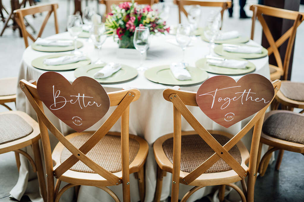 mesa redonda posta com cadeiras de madeira com plaquinhas de coração escrito better toghether