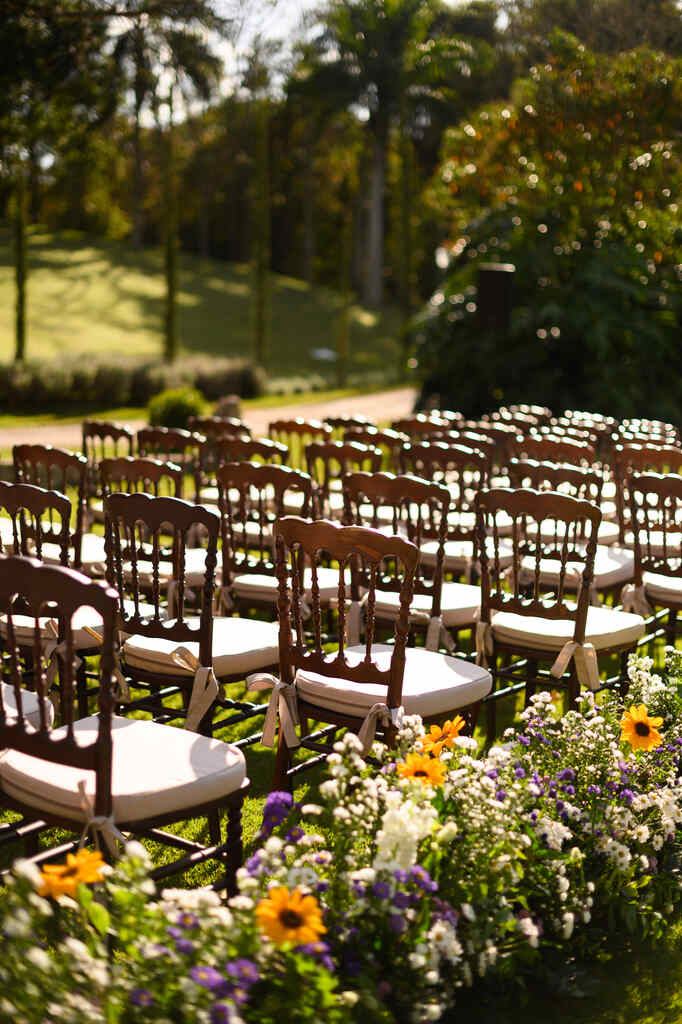 cadeiras de madeira com arranjos com flores brancas roxas e girassois