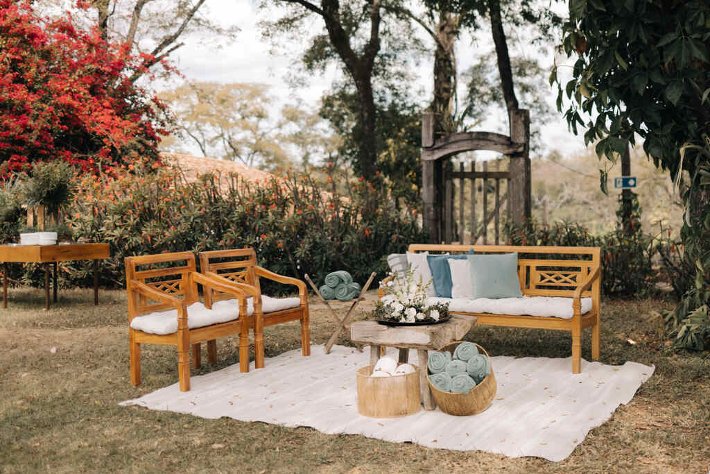 lounge ao ar livre com poltronas e sofá de madeira rústico simples e tapate claro com mesinha e dois cachepôes com tecidos dentro