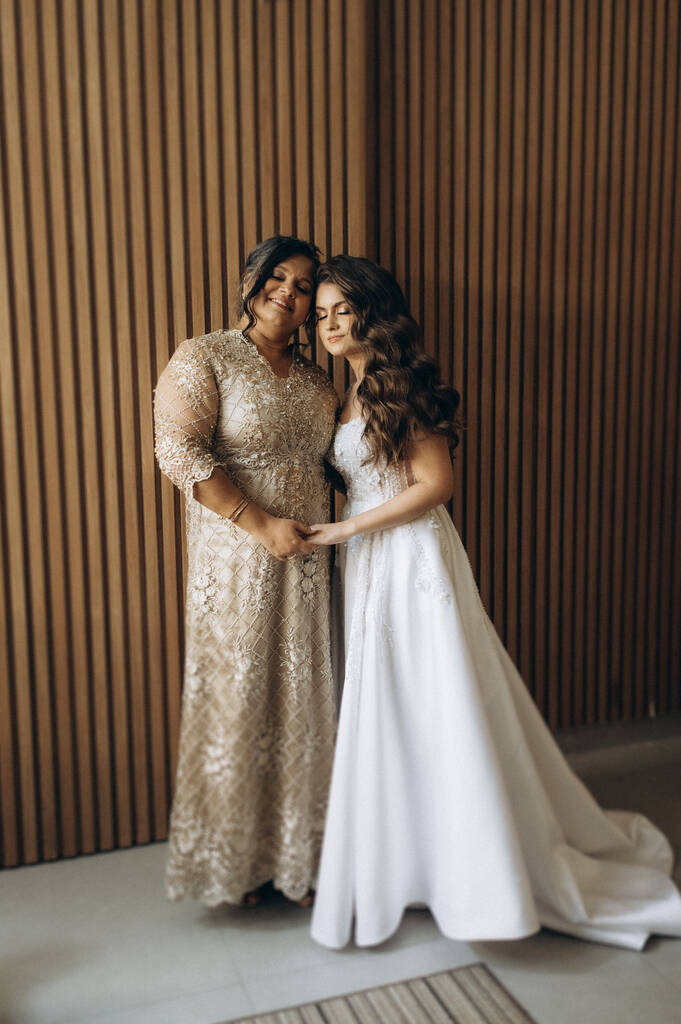 mulher com vetsido de noiva com cauda longa e cabelo ondulado abraçada a mãe com vestido com manga longa brilhante