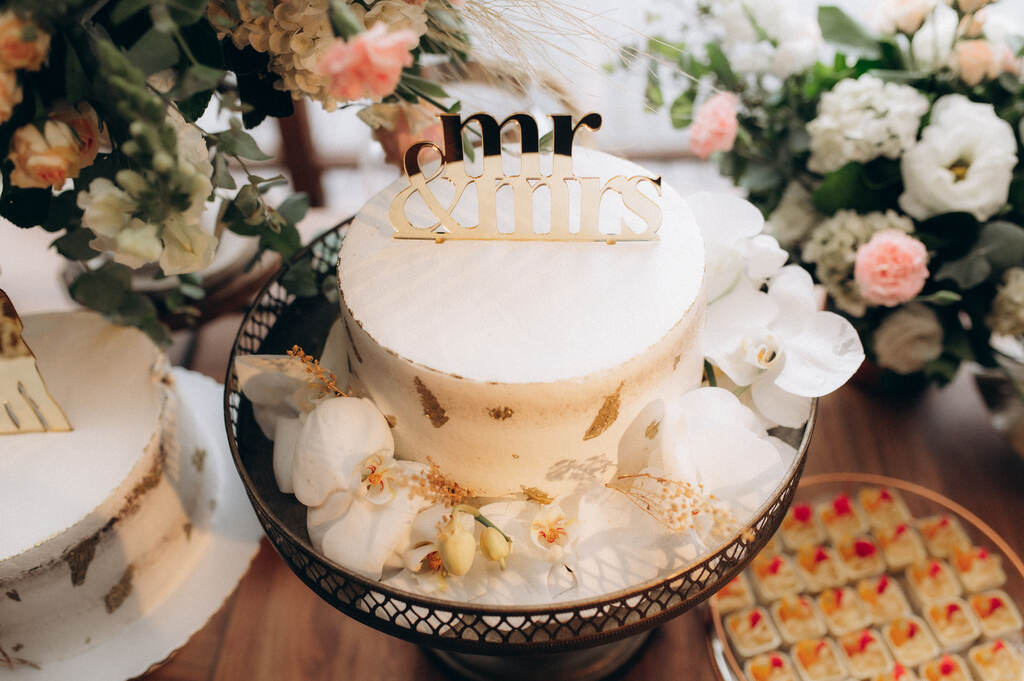 bolo de casamento branco espatulado com orquideas brancas ao lado e topo do bolo escrito mr e mrs dourado