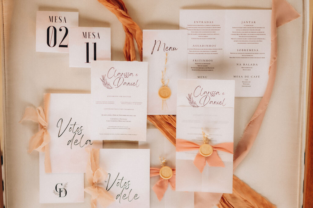 paplearia e convite de casamento branco minimalista com laços cor de rosa e lacre de cera dourado com mini flor sobre a mesa