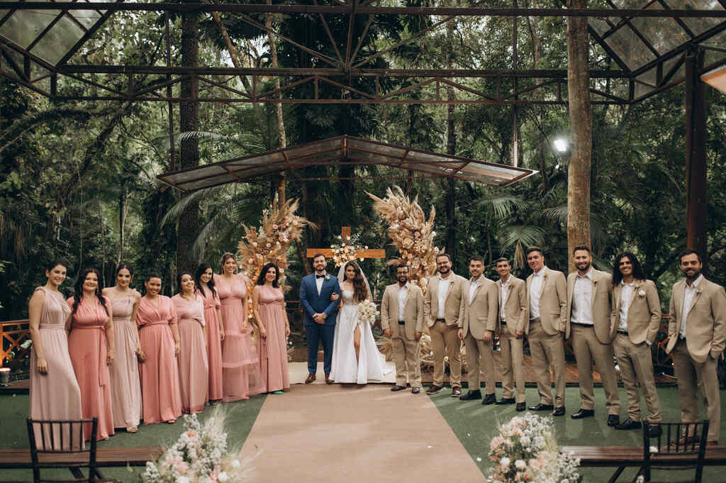 noivos no entro na frente do altar ao lado das madrinhas com vestidos cor de rosa e padrinhos com terno bege